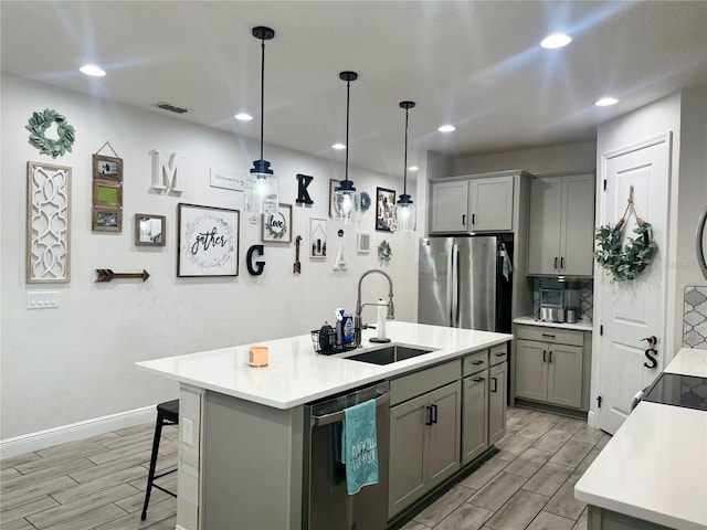 kitchen with pendant lighting, gray cabinetry, appliances with stainless steel finishes, sink, and a center island with sink