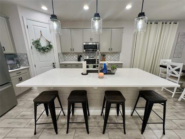 kitchen featuring gray cabinetry, stainless steel appliances, decorative backsplash, and a center island