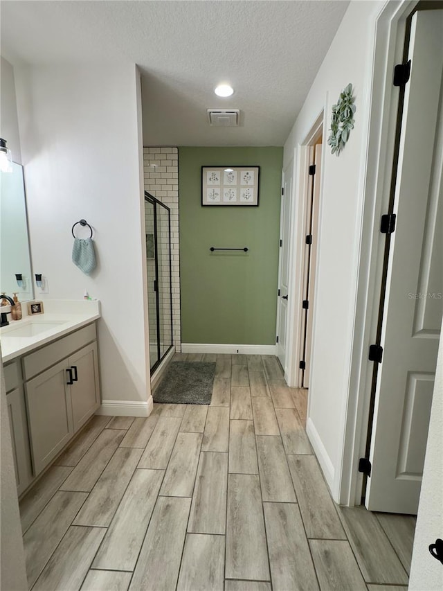 bathroom with a textured ceiling, vanity, walk in shower, and hardwood / wood-style floors