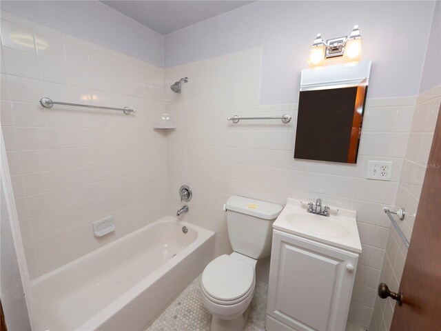 full bathroom featuring vanity, tile patterned flooring, tiled shower / bath combo, toilet, and tile walls