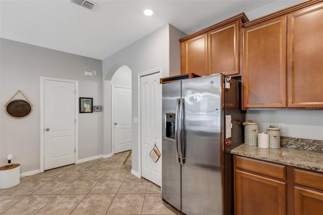 kitchen featuring stainless steel fridge, light tile patterned flooring, and light stone counters