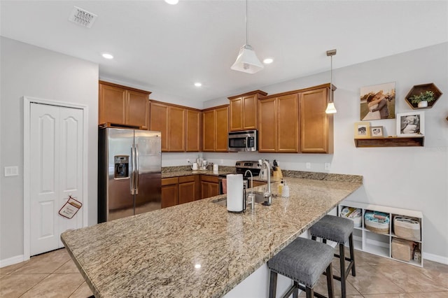 kitchen with light tile patterned flooring, pendant lighting, a kitchen bar, appliances with stainless steel finishes, and kitchen peninsula