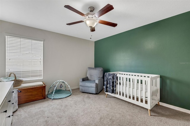 carpeted bedroom with a crib and ceiling fan