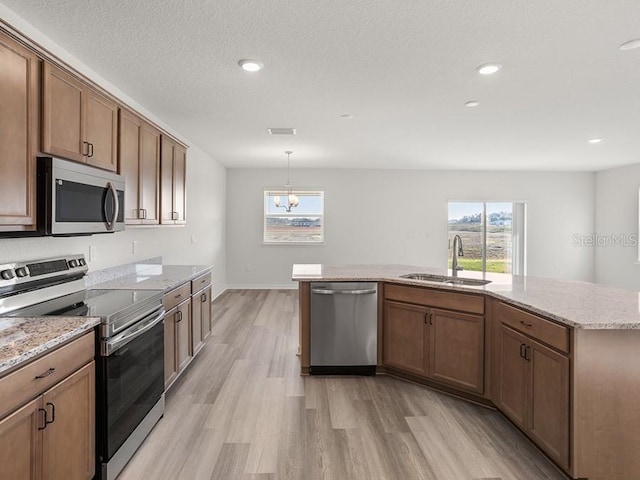 kitchen featuring sink, stainless steel appliances, pendant lighting, light hardwood / wood-style floors, and a kitchen island with sink