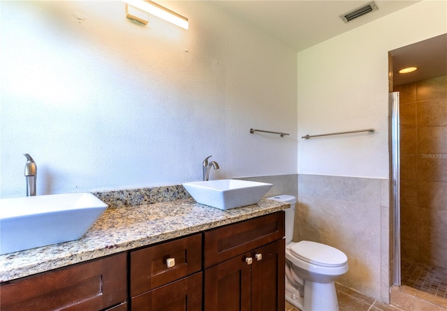 bathroom with tiled shower, tile walls, toilet, tile patterned floors, and vanity