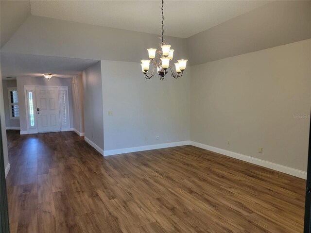 spare room featuring lofted ceiling, dark wood-type flooring, and an inviting chandelier