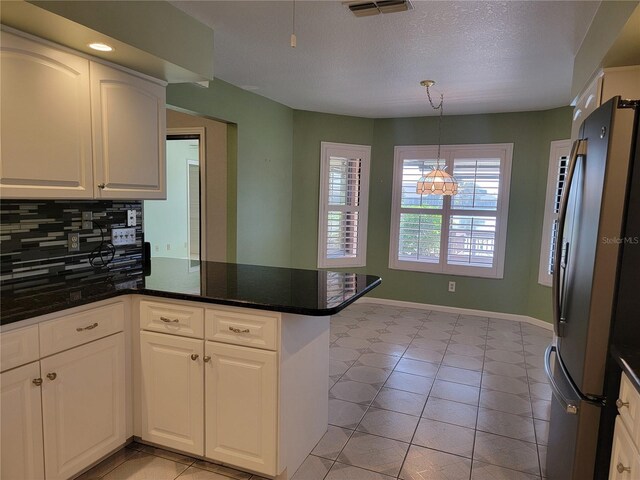 kitchen featuring kitchen peninsula, tasteful backsplash, an inviting chandelier, white cabinetry, and stainless steel refrigerator