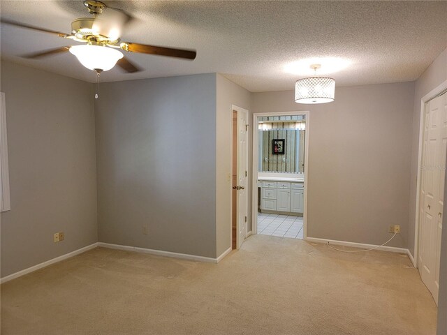 empty room featuring a textured ceiling, light colored carpet, and ceiling fan