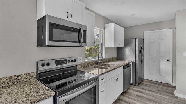 kitchen featuring stainless steel appliances, white cabinets, stone countertops, sink, and light hardwood / wood-style floors