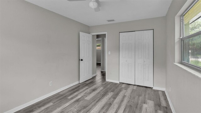 unfurnished bedroom featuring ceiling fan, a closet, wood-type flooring, and multiple windows