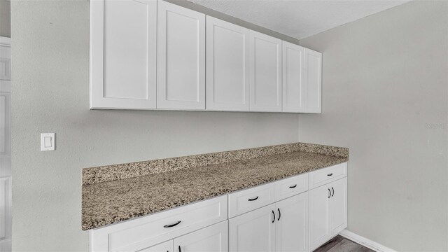 kitchen with white cabinets, hardwood / wood-style flooring, and light stone counters