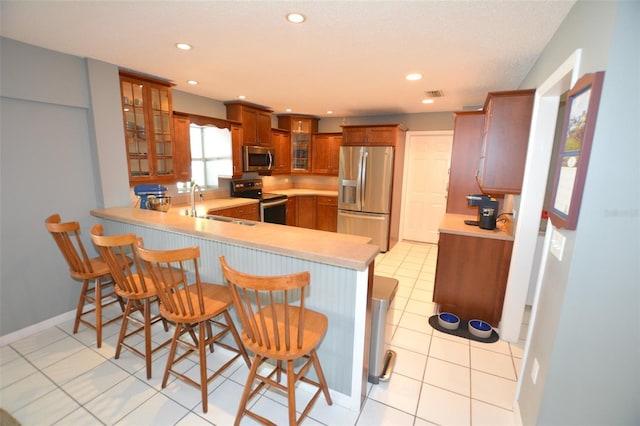 kitchen with a breakfast bar, sink, light tile patterned floors, appliances with stainless steel finishes, and kitchen peninsula