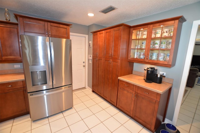 kitchen with stainless steel fridge, light tile patterned floors, and a textured ceiling