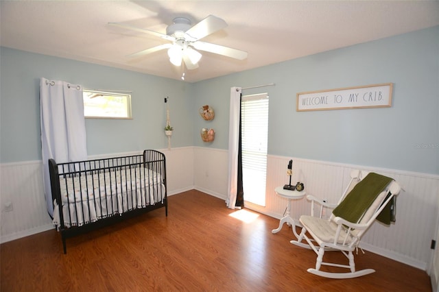 bedroom featuring ceiling fan, hardwood / wood-style floors, and a nursery area