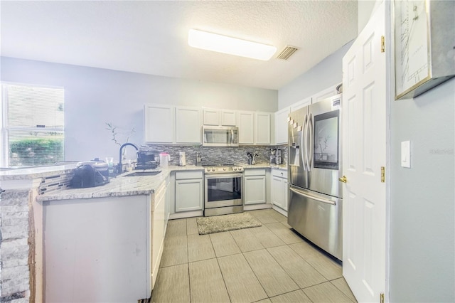 kitchen with white cabinetry, light tile patterned floors, kitchen peninsula, backsplash, and stainless steel appliances