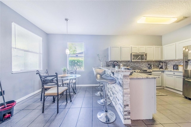 kitchen featuring light tile patterned flooring, backsplash, stainless steel appliances, light stone countertops, and decorative light fixtures