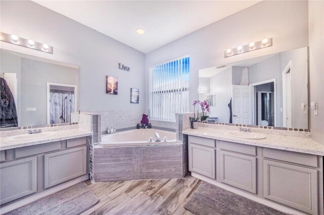 bathroom featuring tiled tub, hardwood / wood-style flooring, and dual bowl vanity