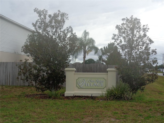 community / neighborhood sign featuring fence and a lawn