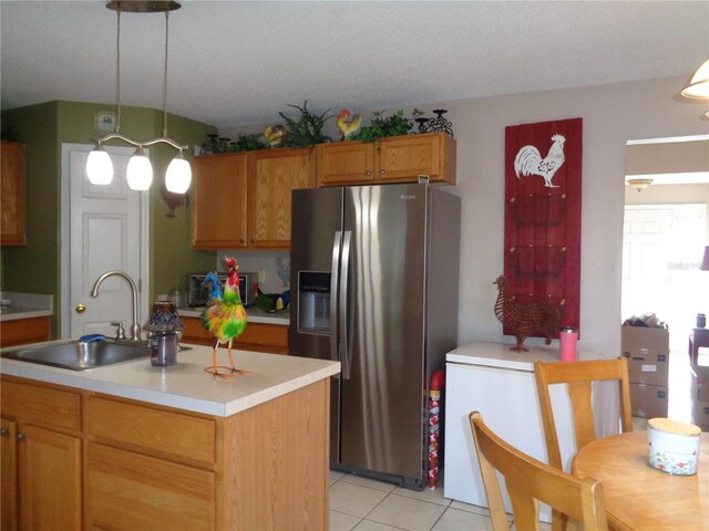 kitchen featuring hanging light fixtures, stainless steel refrigerator with ice dispenser, sink, light tile patterned floors, and a kitchen island with sink