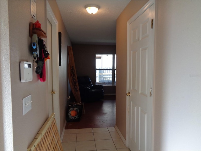 hallway with radiator, light tile patterned floors, baseboards, and a textured ceiling