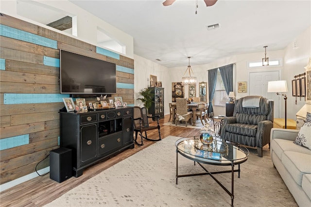 living room featuring hardwood / wood-style floors, ceiling fan with notable chandelier, and wood walls