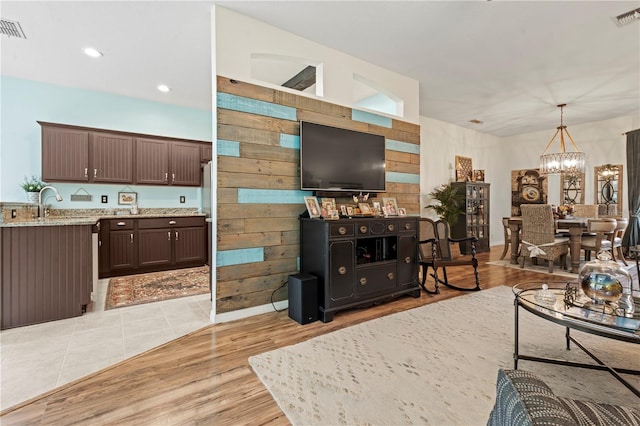 living room with a notable chandelier, wooden walls, and light hardwood / wood-style floors