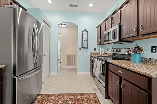 kitchen with stainless steel appliances, dark brown cabinets, and light stone countertops