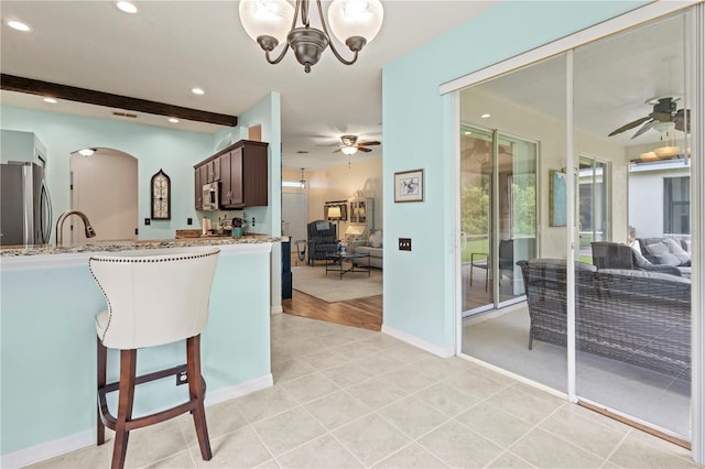 kitchen with light stone countertops, appliances with stainless steel finishes, ceiling fan with notable chandelier, and dark brown cabinets