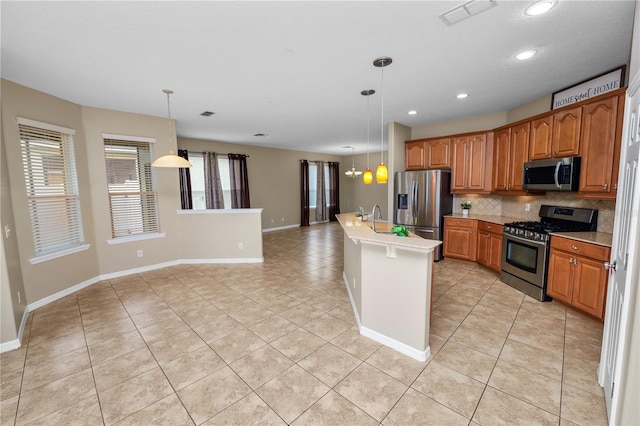 kitchen with light tile patterned floors, stainless steel appliances, tasteful backsplash, an island with sink, and decorative light fixtures