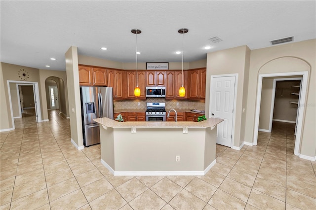 kitchen with a breakfast bar, tasteful backsplash, a center island with sink, appliances with stainless steel finishes, and pendant lighting