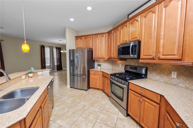 kitchen with pendant lighting, sink, stainless steel appliances, and light stone countertops