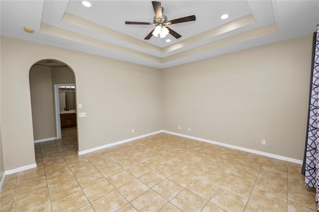 empty room featuring a raised ceiling, light tile patterned floors, and ceiling fan