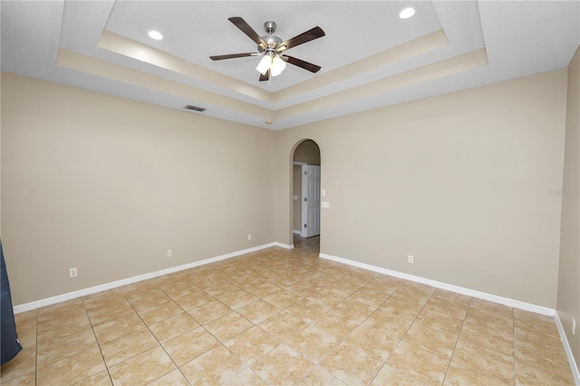 tiled empty room with ceiling fan and a tray ceiling