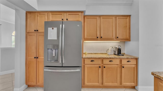 kitchen featuring light tile patterned floors, stainless steel fridge, light stone countertops, and light brown cabinets