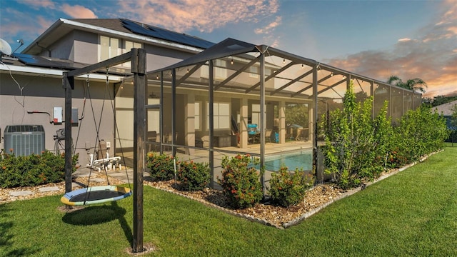 back house at dusk with a patio, a trampoline, a lanai, a yard, and central air condition unit