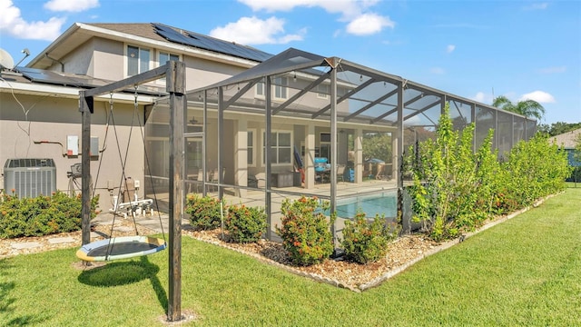 rear view of house with a lawn, glass enclosure, central air condition unit, a patio area, and solar panels