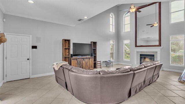 tiled living room with a high ceiling, ceiling fan, crown molding, and a fireplace