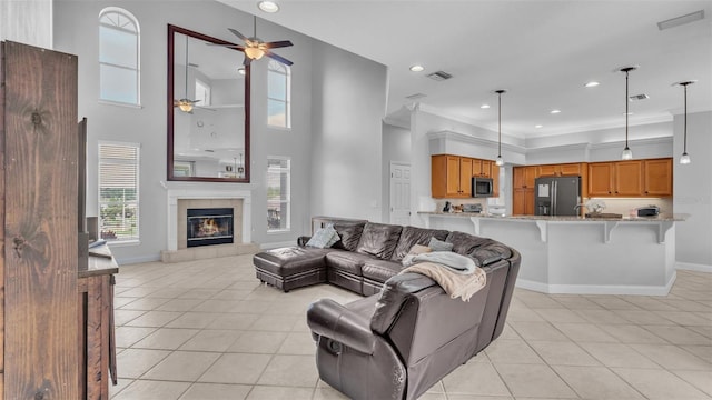 tiled living room with crown molding, a towering ceiling, ceiling fan, and a fireplace