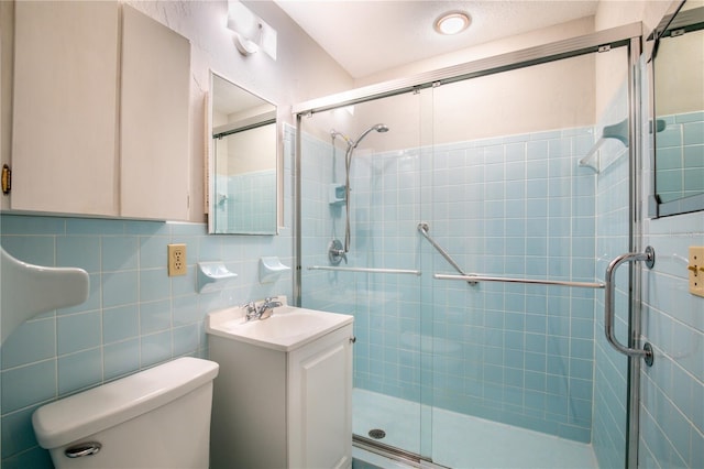 bathroom with vanity, a shower with door, toilet, and tile walls