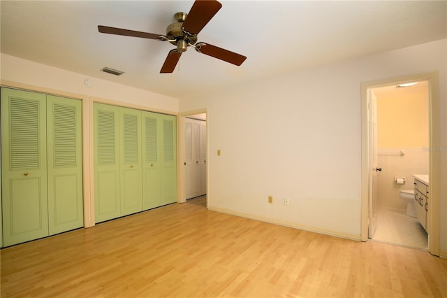 unfurnished bedroom with ensuite bath, light hardwood / wood-style flooring, tile walls, multiple closets, and ceiling fan