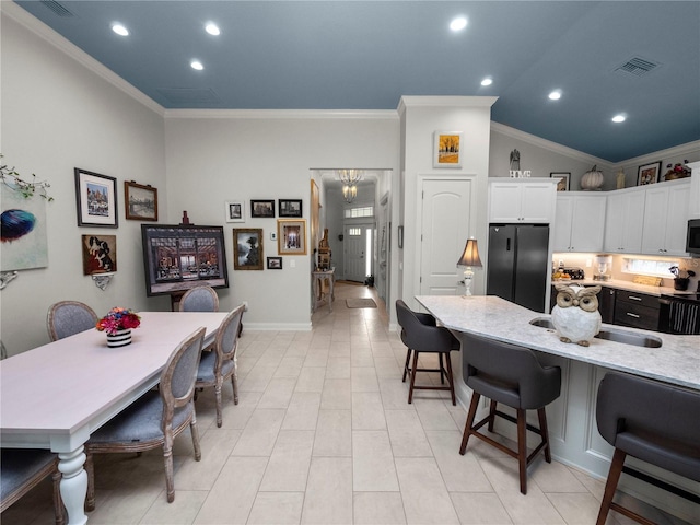 kitchen with lofted ceiling, a kitchen breakfast bar, ornamental molding, black refrigerator, and white cabinets