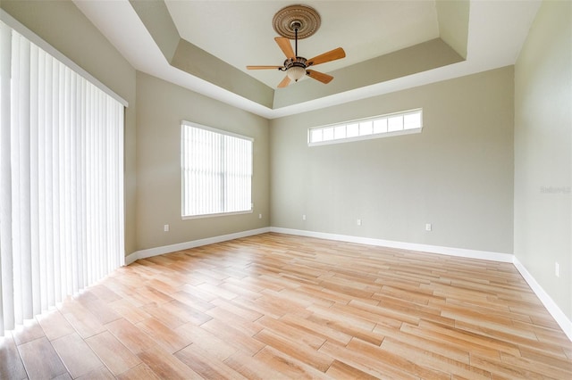 unfurnished room featuring a raised ceiling, ceiling fan, and light hardwood / wood-style floors