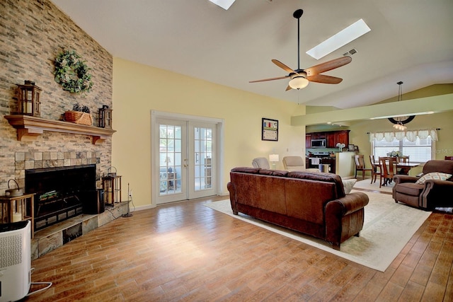 living room with french doors, a tiled fireplace, lofted ceiling with skylight, ceiling fan, and wood-type flooring