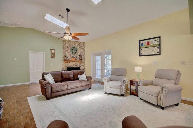 living room with ceiling fan, hardwood / wood-style flooring, a brick fireplace, and vaulted ceiling with skylight