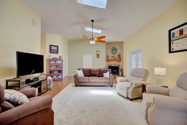 living room with a fireplace, lofted ceiling with skylight, hardwood / wood-style flooring, and ceiling fan