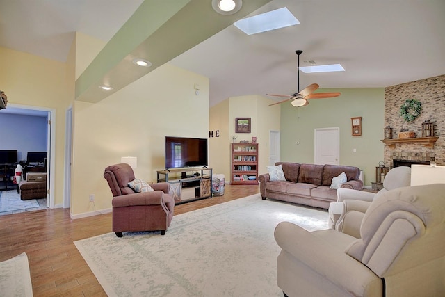 living room with wood-type flooring, ceiling fan, high vaulted ceiling, a skylight, and a brick fireplace