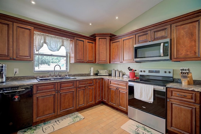 kitchen featuring lofted ceiling, stone counters, appliances with stainless steel finishes, and sink