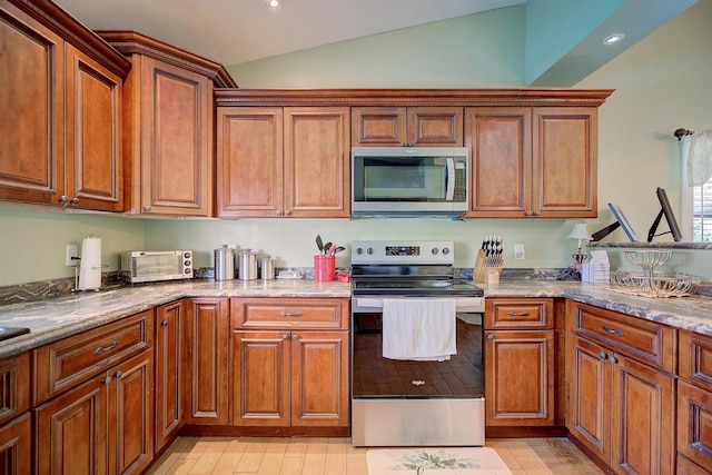 kitchen with lofted ceiling, light stone countertops, stainless steel appliances, and light hardwood / wood-style floors