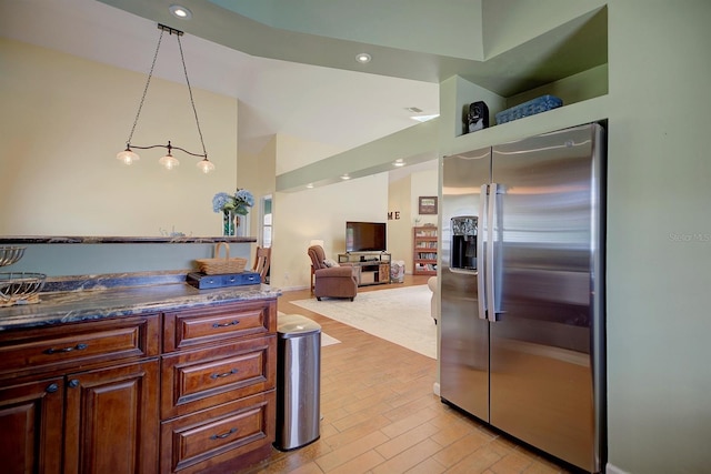 kitchen with stainless steel fridge, dark stone countertops, decorative light fixtures, and light wood-type flooring