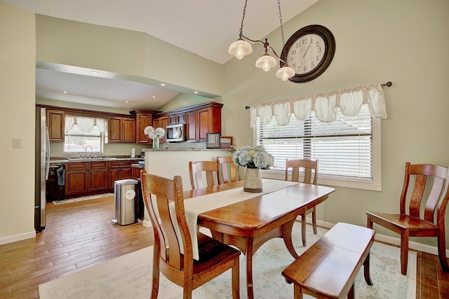 dining space with light hardwood / wood-style floors, vaulted ceiling, sink, and a wealth of natural light